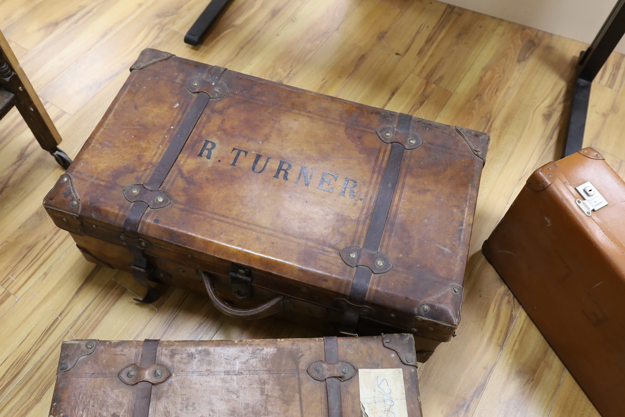 Three early 20th century brown leather cabin trunks and a later vintage suitcase, largest trunk 92cms wide x 52cms deep